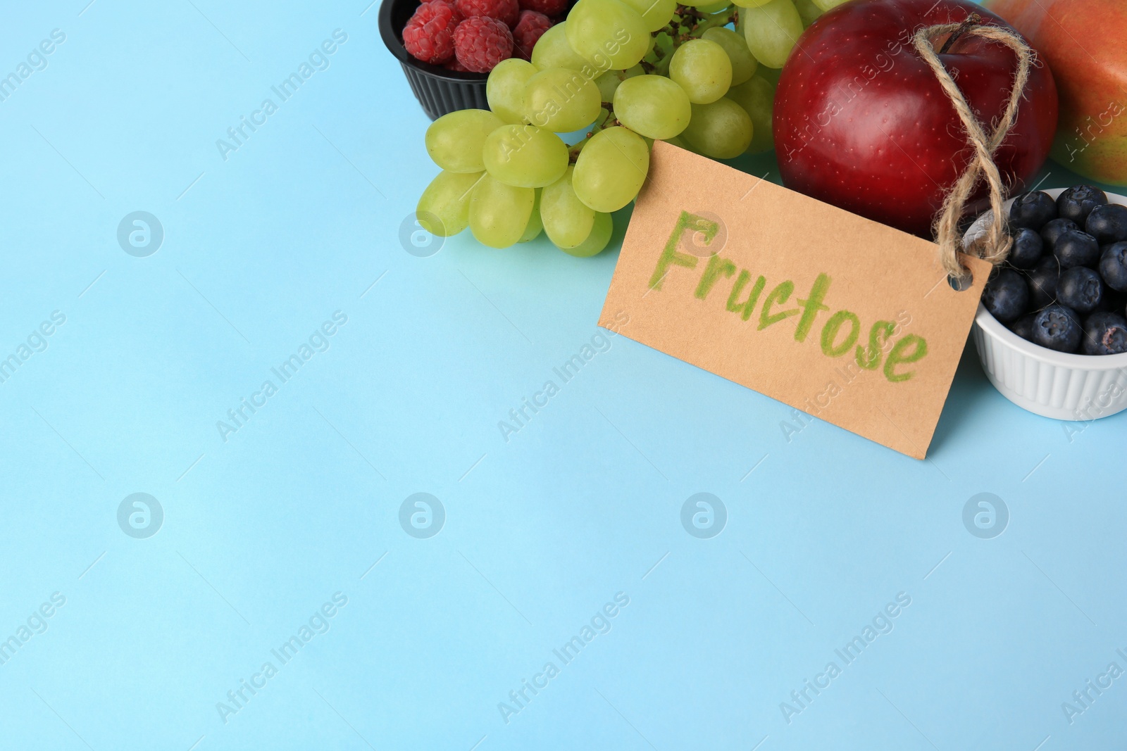 Photo of Card with word Fructose, delicious ripe fruits and berries on light blue background, space for text