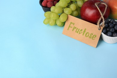 Photo of Card with word Fructose, delicious ripe fruits and berries on light blue background, space for text