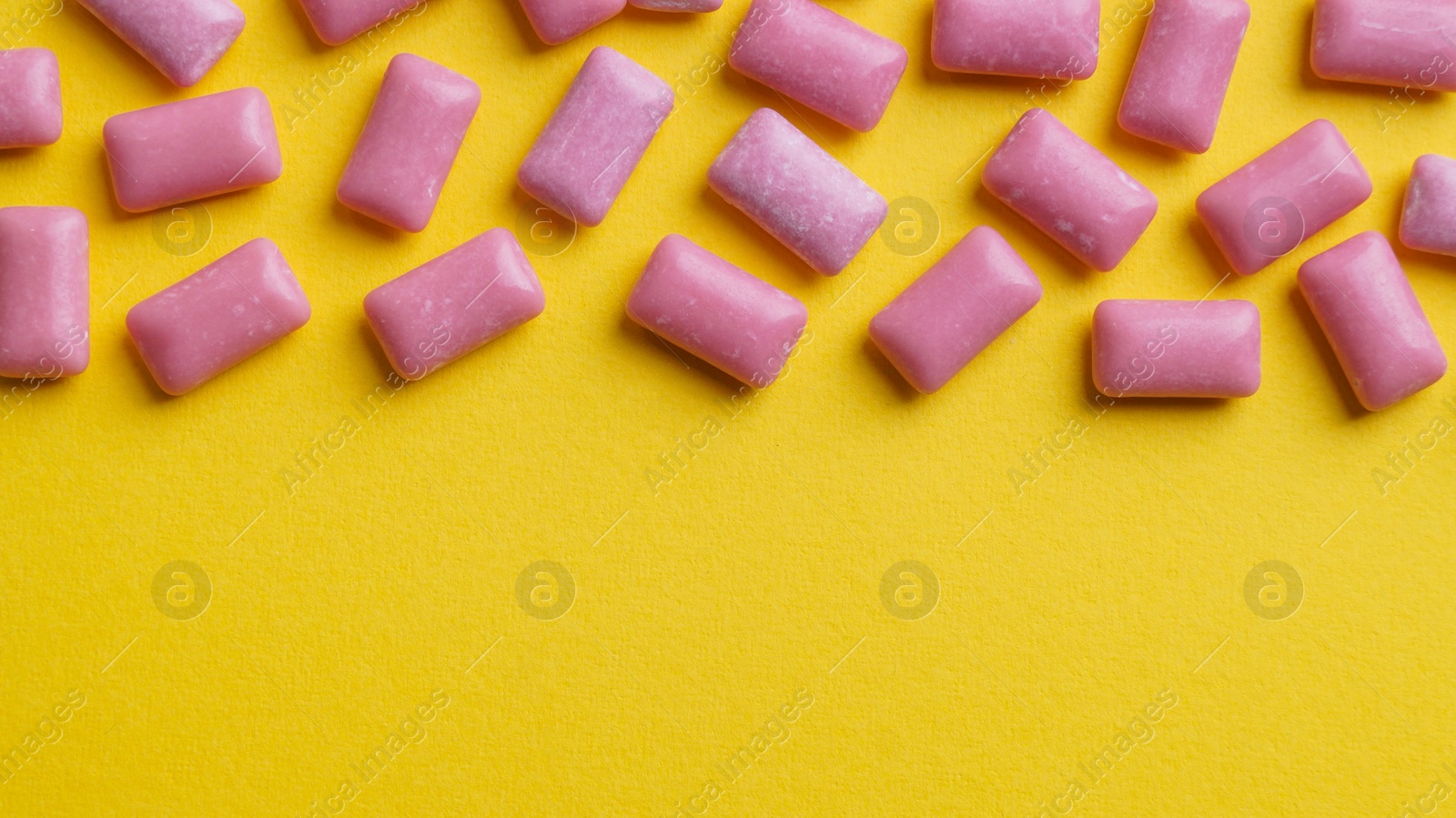 Photo of Sweet chewing gums on yellow background, flat lay. Space for text