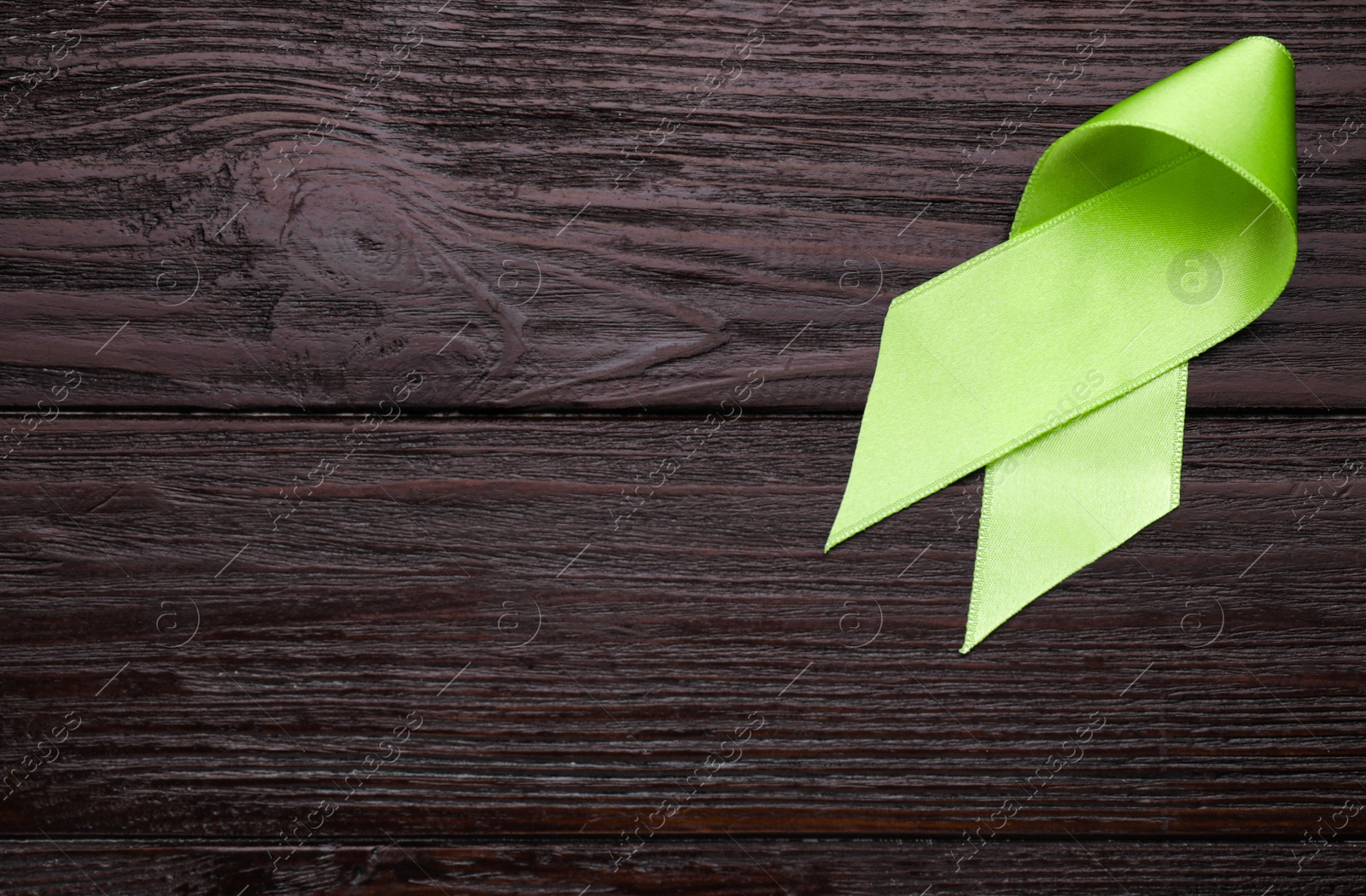 Photo of World Mental Health Day. Green ribbon on wooden background, top view with space for text