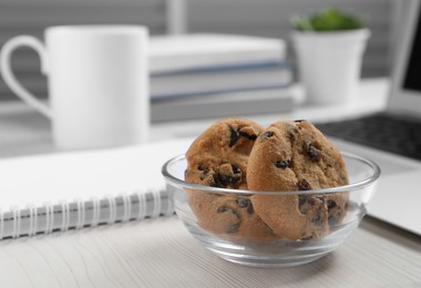 Photo of Bowl with chocolate chip cookies on white wooden table in office, closeup. Space for text
