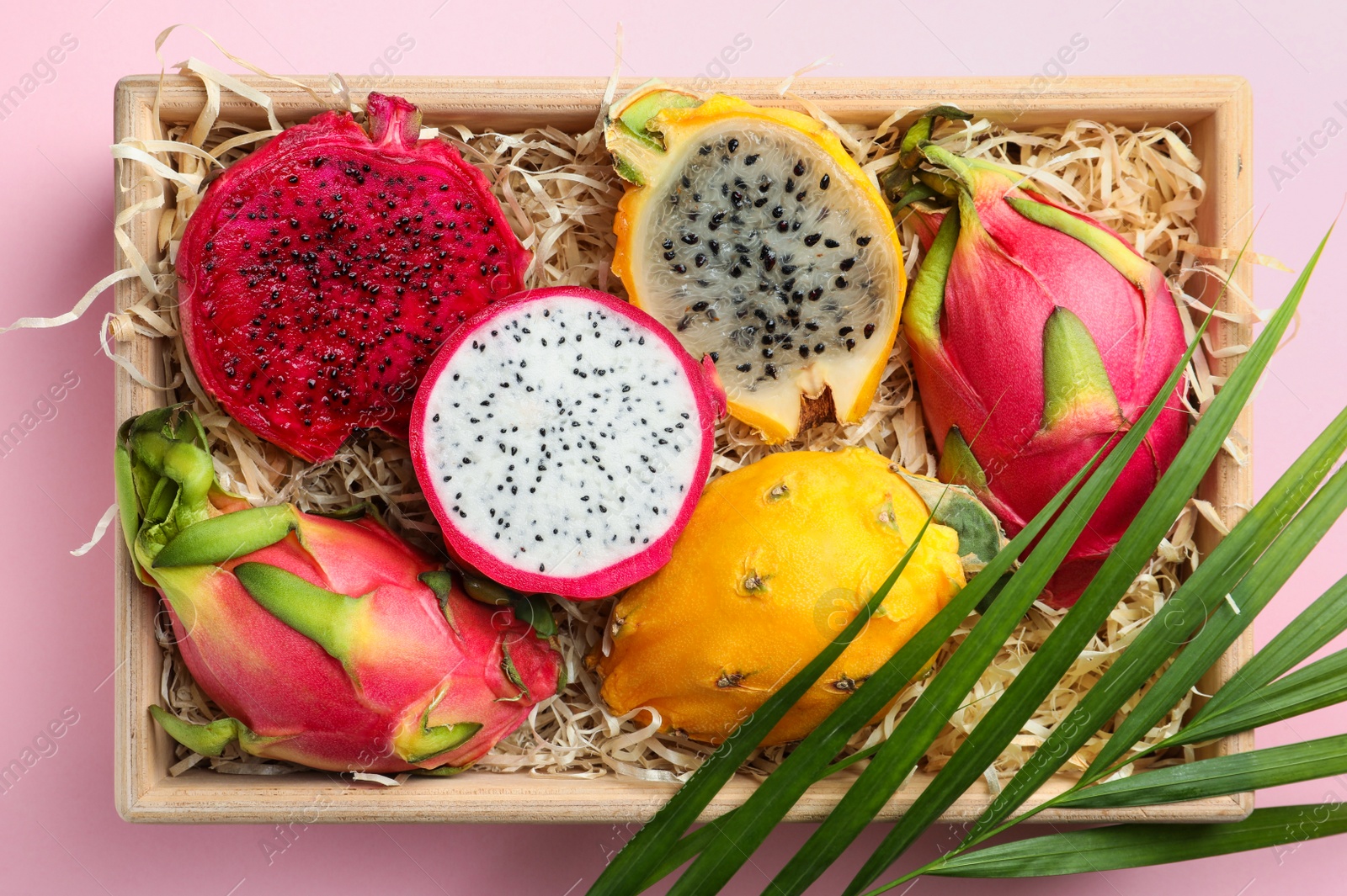 Photo of Delicious cut and whole dragon fruits in crate on pink background, top view