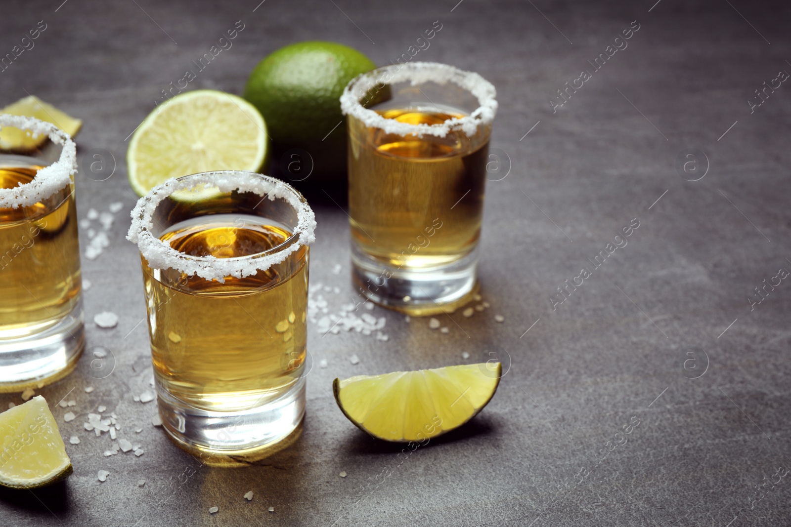 Photo of Mexican Tequila shots, lime slices and salt on grey table