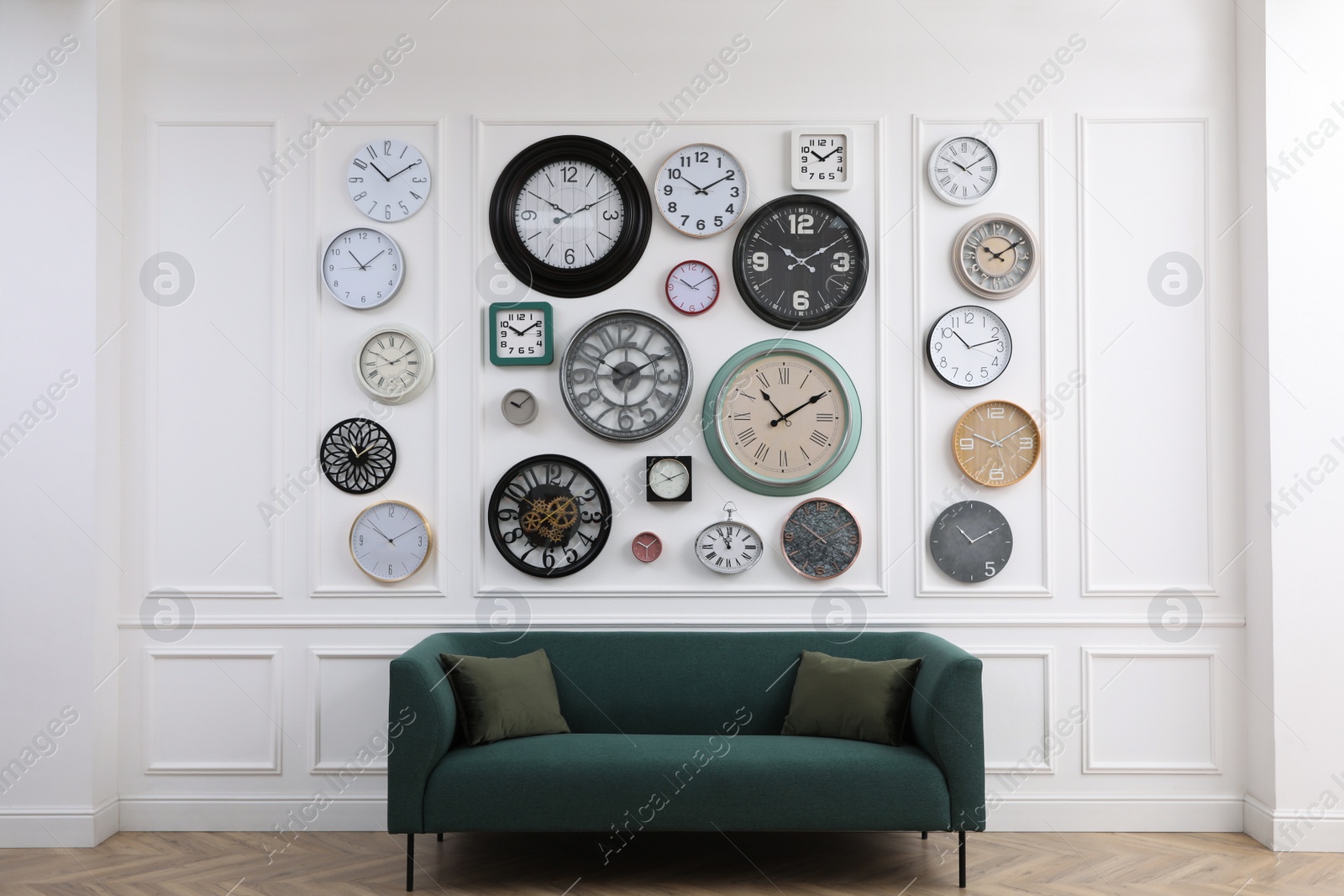 Photo of Collection of different clocks and comfortable sofa in stylish room. Interior design