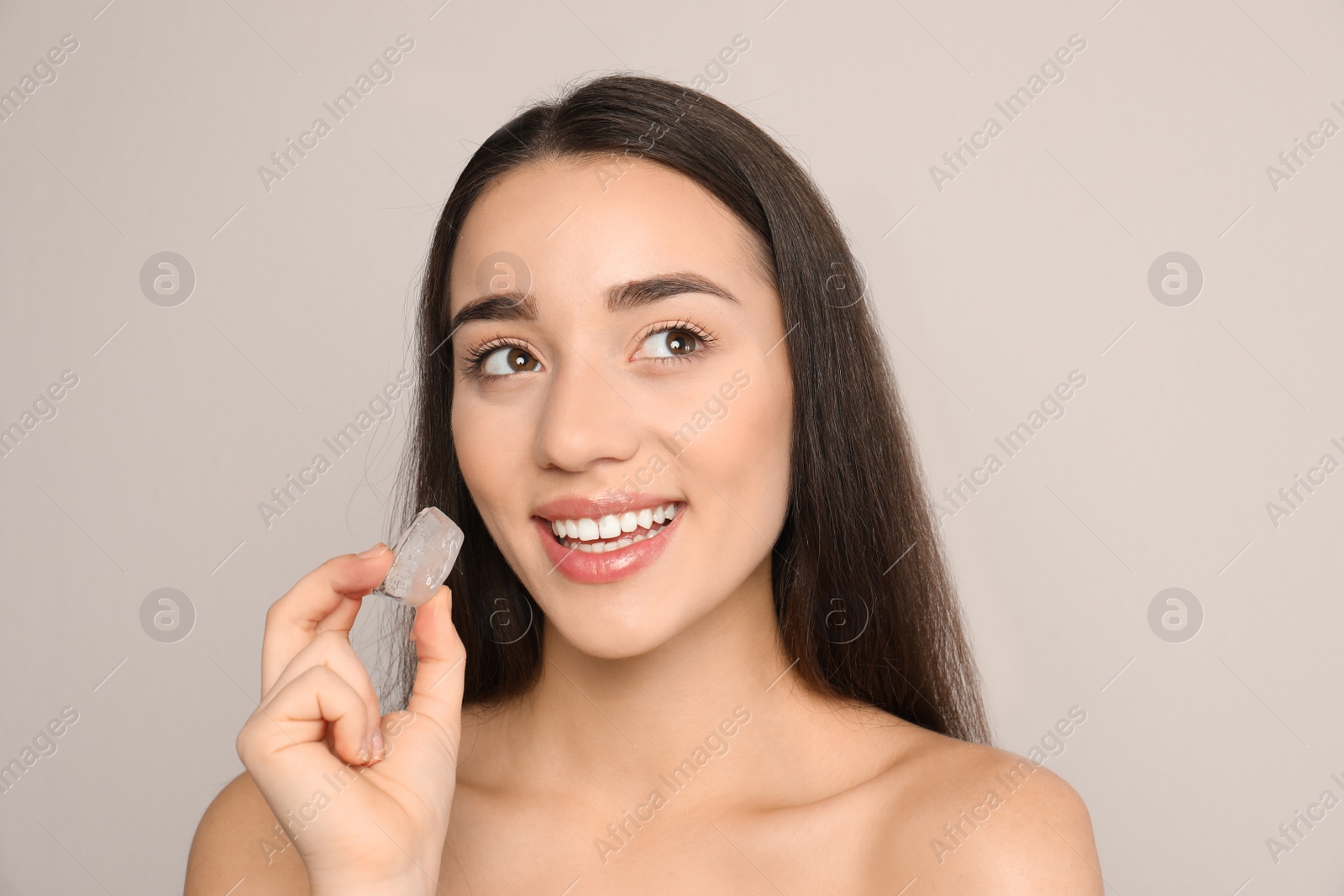 Photo of Young woman with ice cube on light background. Skin care