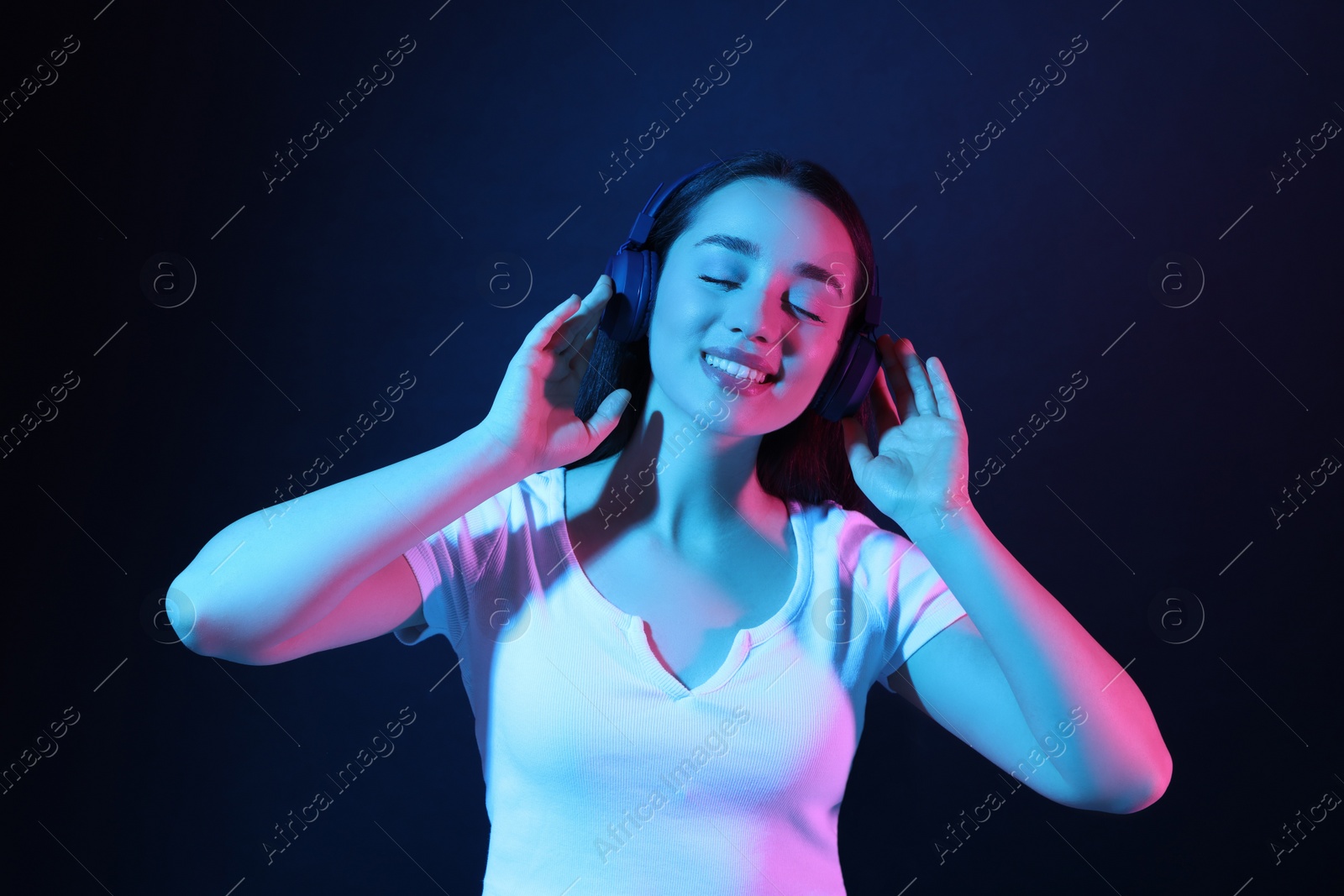 Photo of Happy woman in headphones enjoying music in neon lights against dark blue background