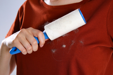 Photo of Woman removing cat hair from red t-shirt with lint roller on grey background, closeup