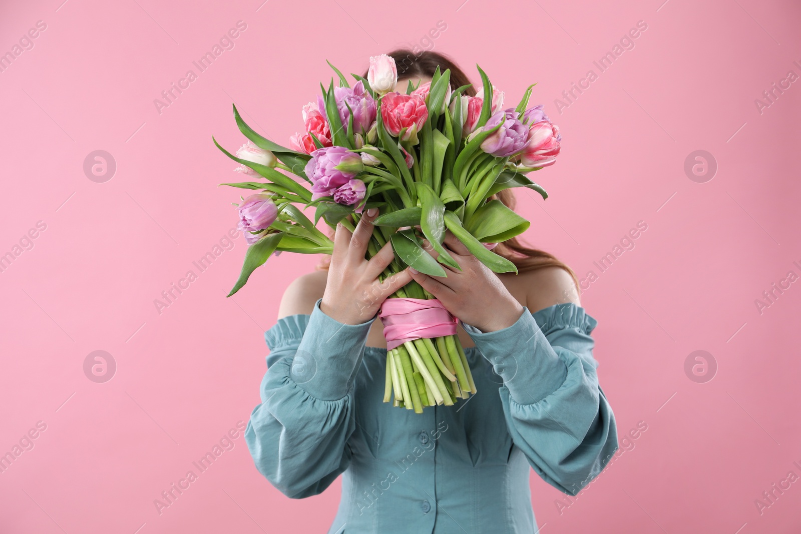 Photo of Woman covering her face with bouquet of beautiful tulips on pink background