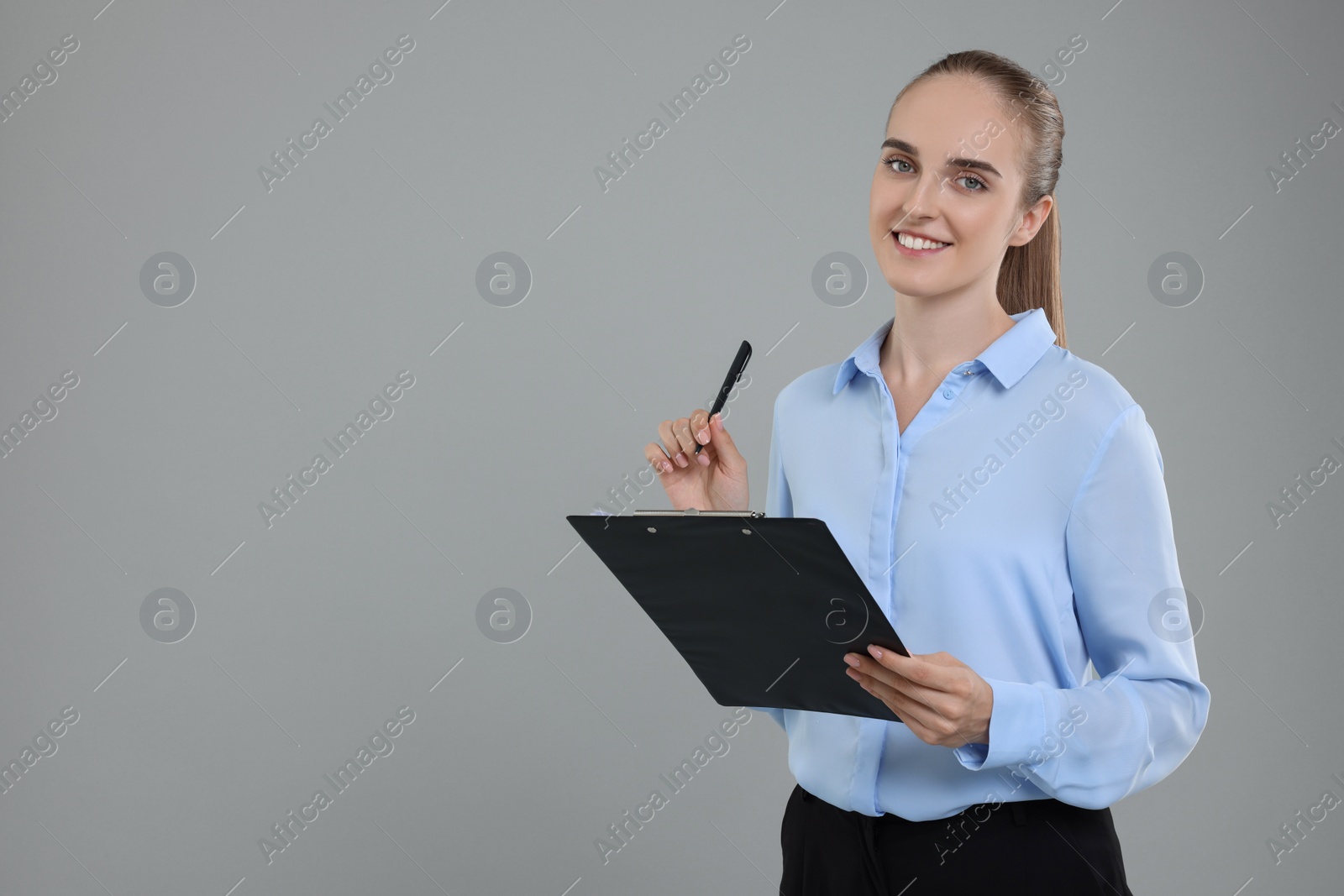 Photo of Happy young secretary with clipboard and pen on grey background, space for text