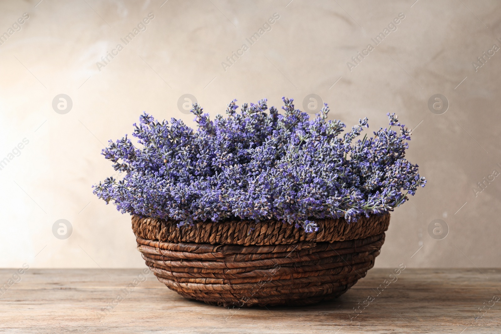 Photo of Fresh lavender flowers in basket on wooden table against beige background