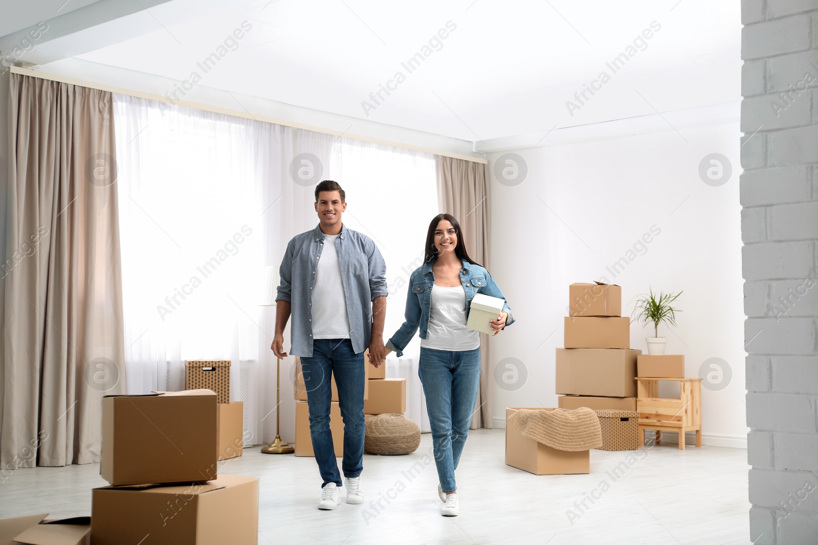 Photo of Happy couple in room with cardboard boxes on moving day