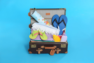 Photo of Open vintage suitcase with different beach objects packed for summer vacation on light blue background