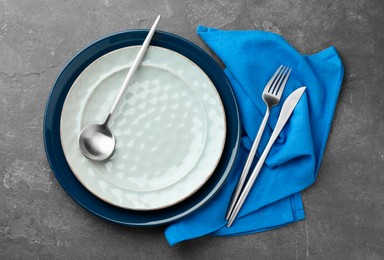 Photo of Stylish setting with cutlery, plates and napkin on grey textured table, flat lay