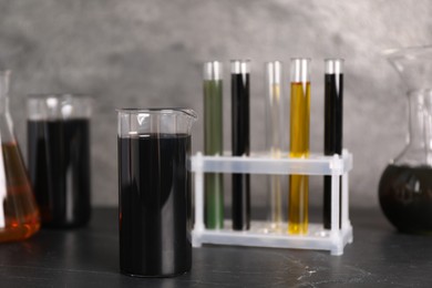 Beakers, flasks and test tubes with different types of oil on grey textured table, closeup