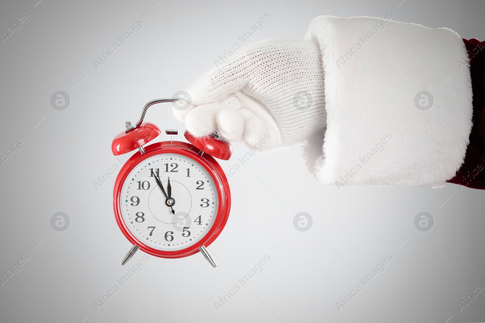 Photo of Santa Claus holding alarm clock on light grey background, closeup. Christmas countdown