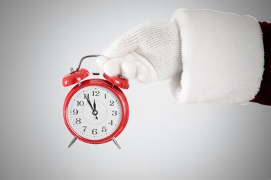 Photo of Santa Claus holding alarm clock on light grey background, closeup. Christmas countdown