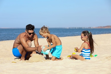 Father and children playing on sandy beach near sea. Summer holidays with family