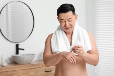 Photo of Handsome man applying body cream onto his hand in bathroom. Space for text