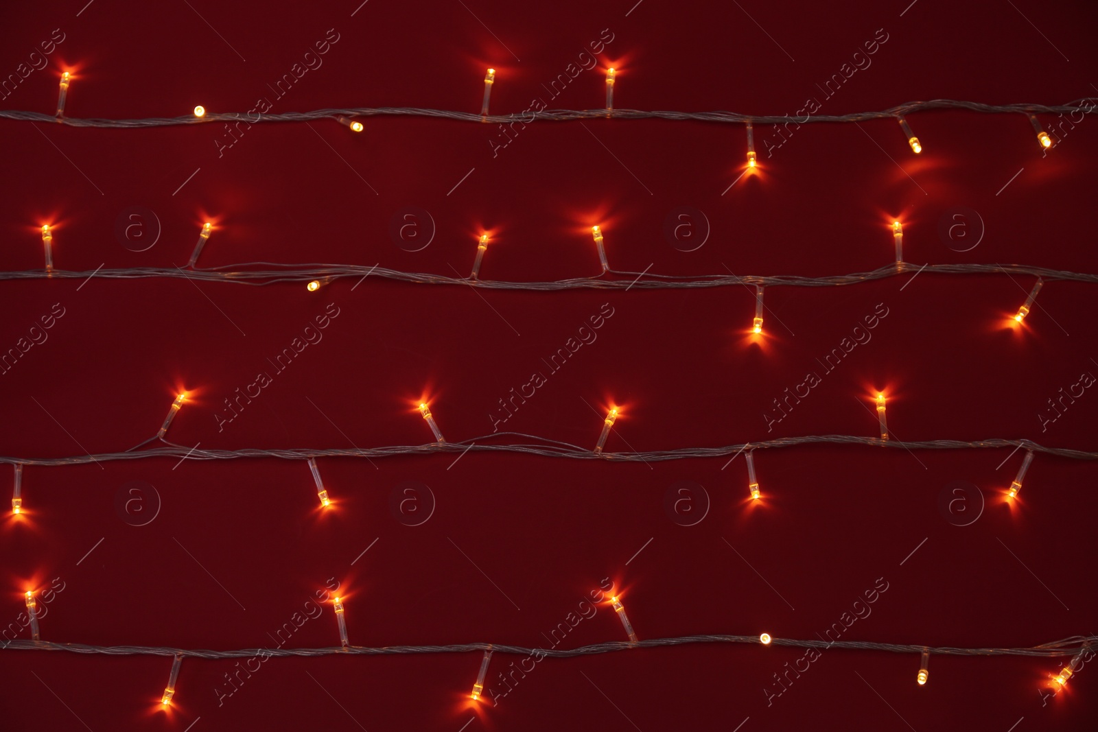 Photo of Glowing Christmas lights on red background, top view