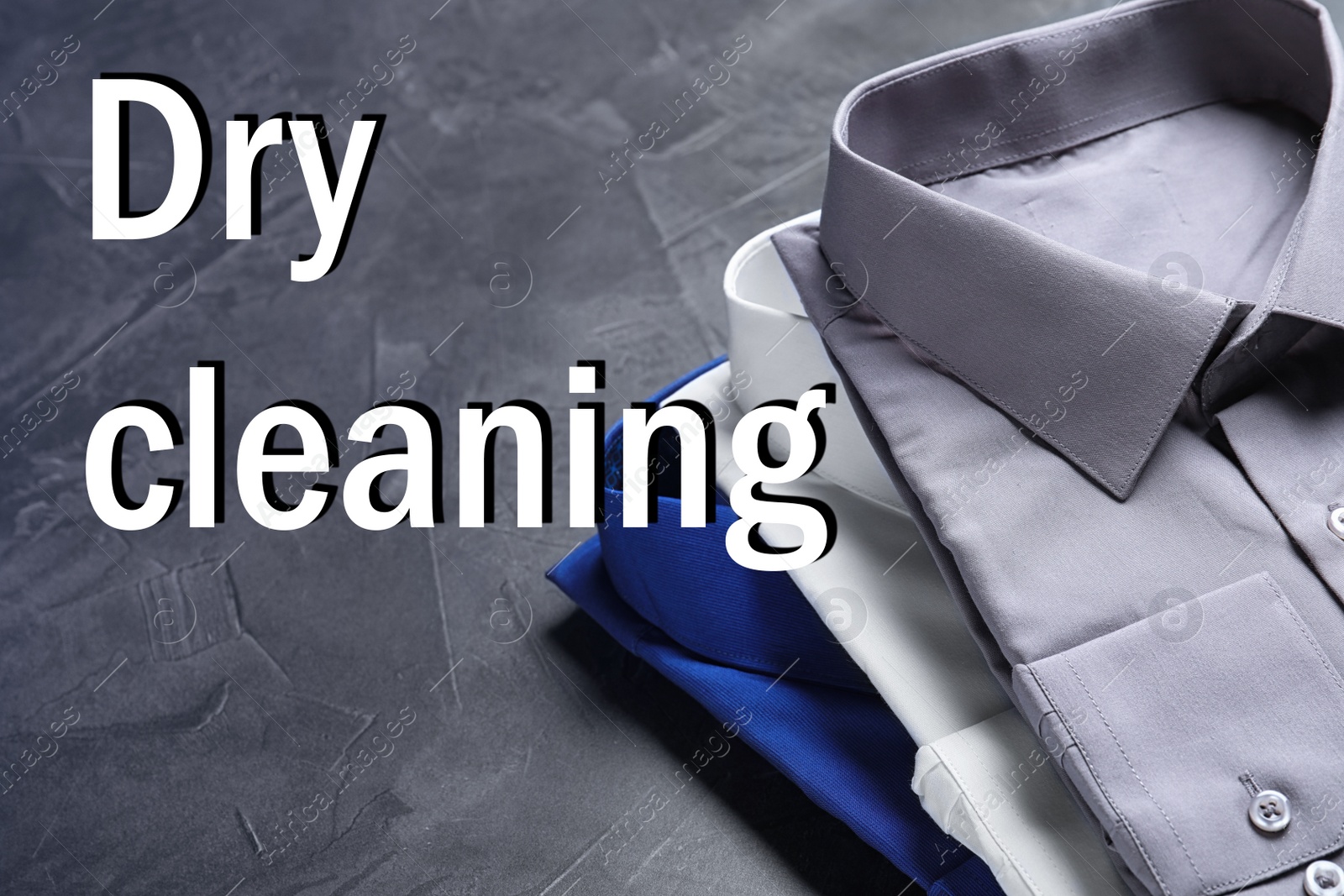 Image of Stylish shirts on grey stone table and inscription Dry Cleaning 