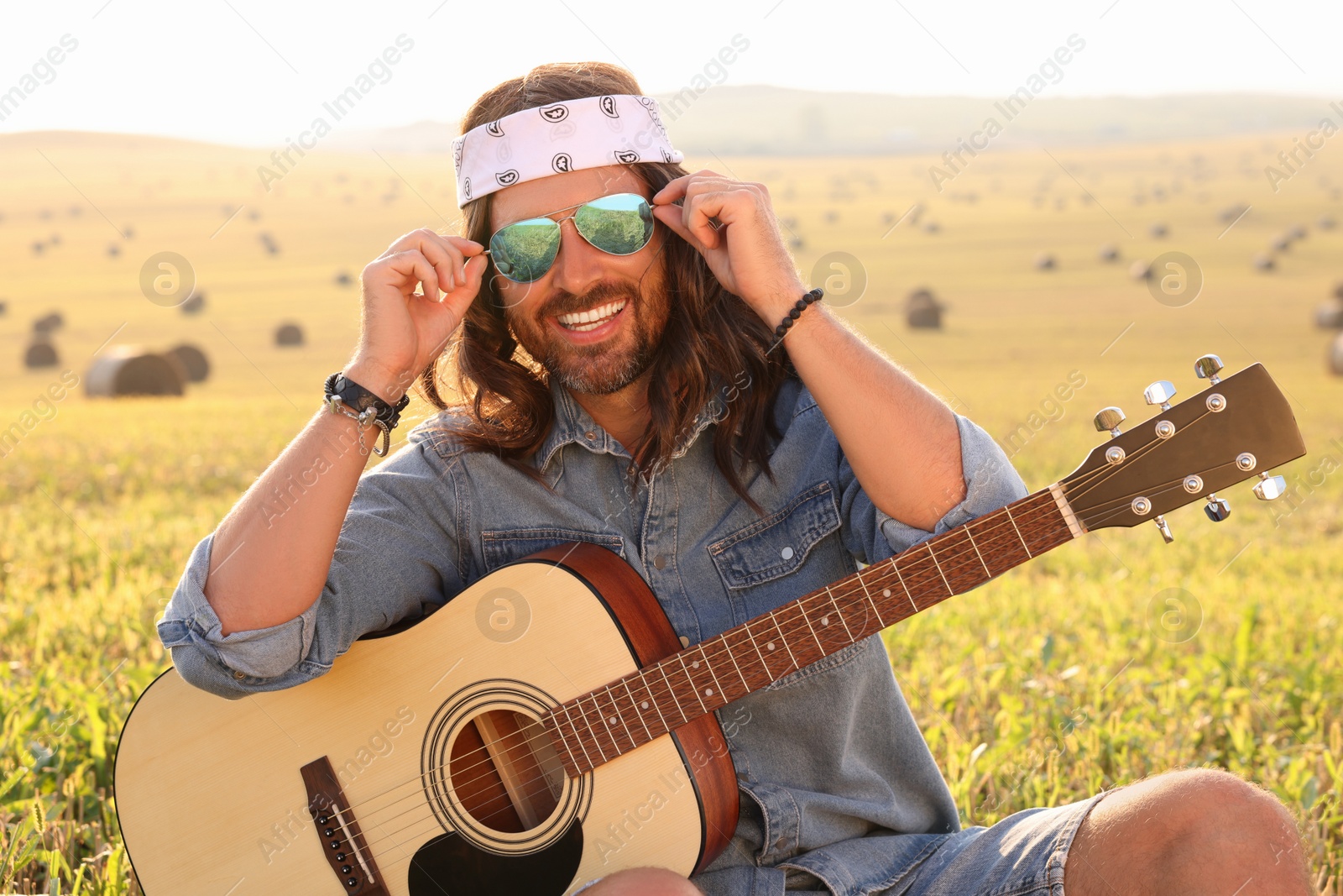 Photo of Portrait of happy hippie man with guitar in field