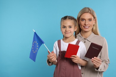 Photo of Immigration. Happy woman with her daughter holding passports and flag of European Union on light blue background