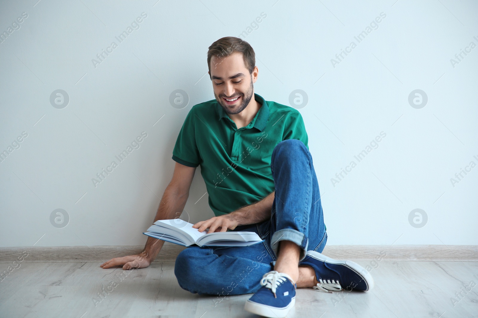 Photo of Young man reading book on floor near wall