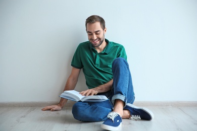 Photo of Young man reading book on floor near wall