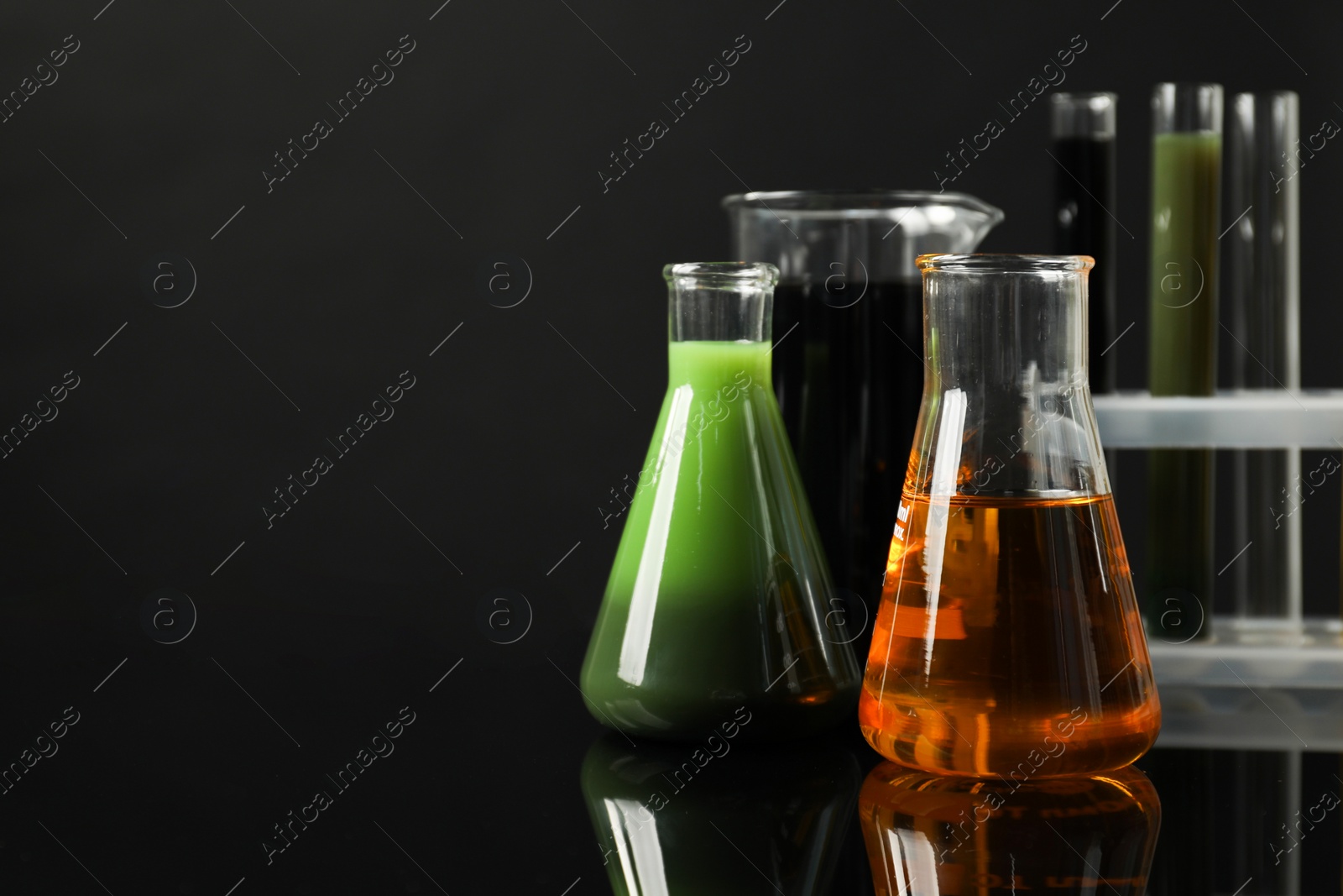 Photo of Laboratory glassware with different types of oil on black background, space for text