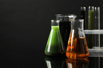 Laboratory glassware with different types of oil on black background, space for text