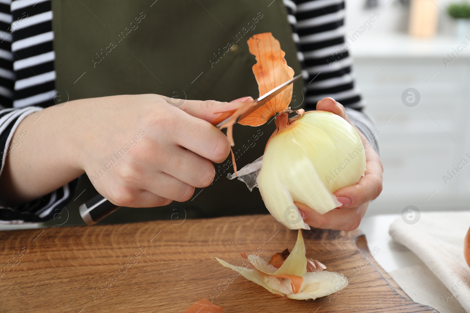 Photo of Woman peeling fresh onion with knife at table indoors, closeup