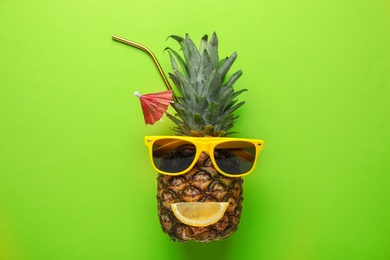 Photo of Pineapple with funny face made of sunglasses and citrus slice as summer cocktail on color background, top view