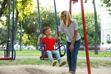 Photo of Nanny and cute little boy on swing in park