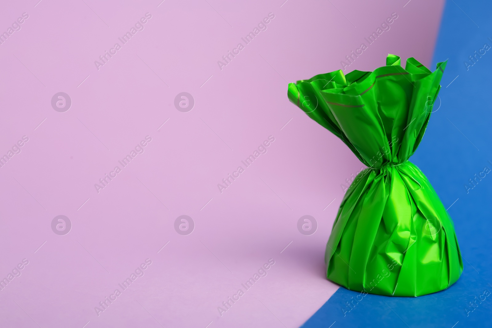 Photo of Candy in green wrapper on color background. Space for text