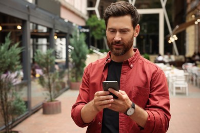 Handsome man using smartphone on city street, space for text