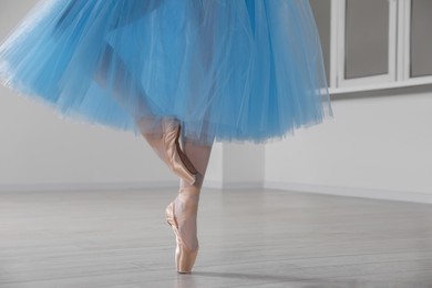 Photo of Ballerina in pointe shoes and light blue skirt dancing indoors, closeup