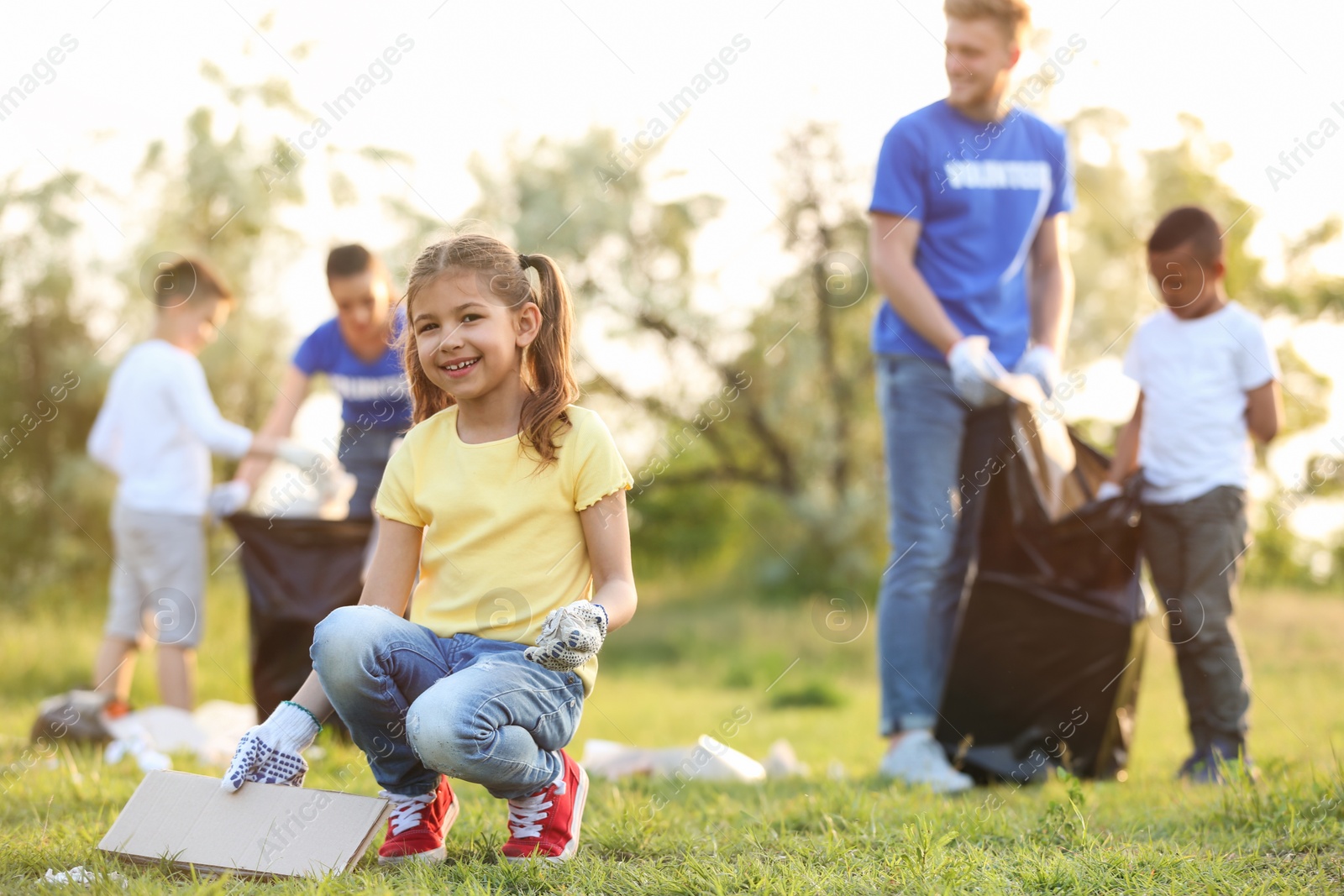 Photo of Little girl collecting trash in park. Volunteer project