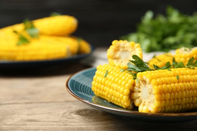 Photo of Plate of boiled corn cobs with parsley on wooden table, closeup. Space for text