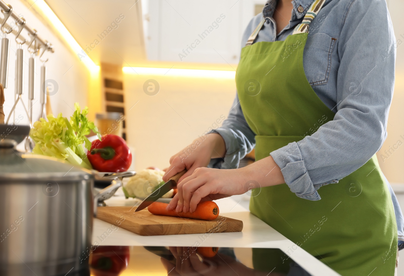 Photo of Woman cutting carrot to make bouillon in kitchen, closeup. Homemade recipe