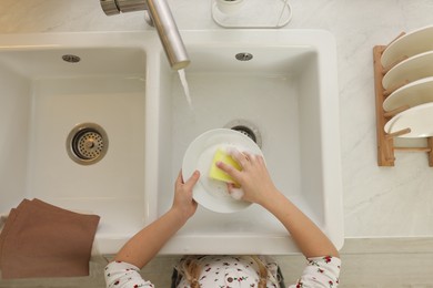 Girl washing plate above sink in kitchen, top view