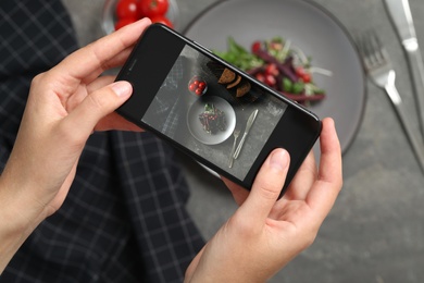 Blogger taking picture of salad at grey table, top view