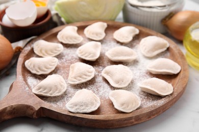 Raw dumplings (varenyky) with tasty filling and flour on wooden board, closeup