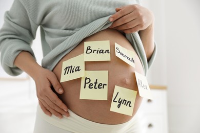 Photo of Pregnant woman with different baby names on belly indoors, closeup