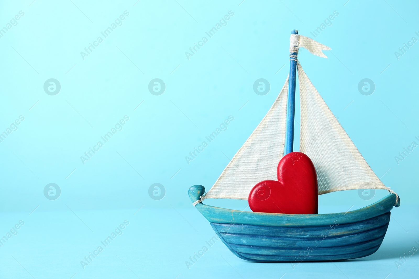 Photo of Toy ship with red decorative heart on color background. Space for text