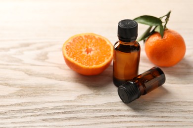 Bottles of tangerine essential oil and fresh fruits on wooden table. Space for text