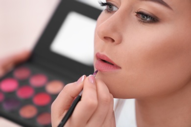 Photo of Professional visage artist applying makeup on woman's face in salon, closeup