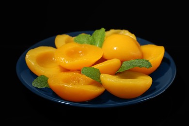 Photo of Plate with canned peach halves on black background