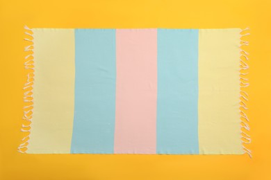 Striped beach towel on yellow background, top view