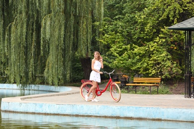 Beautiful woman in casual outfit with bicycle near pond outdoors