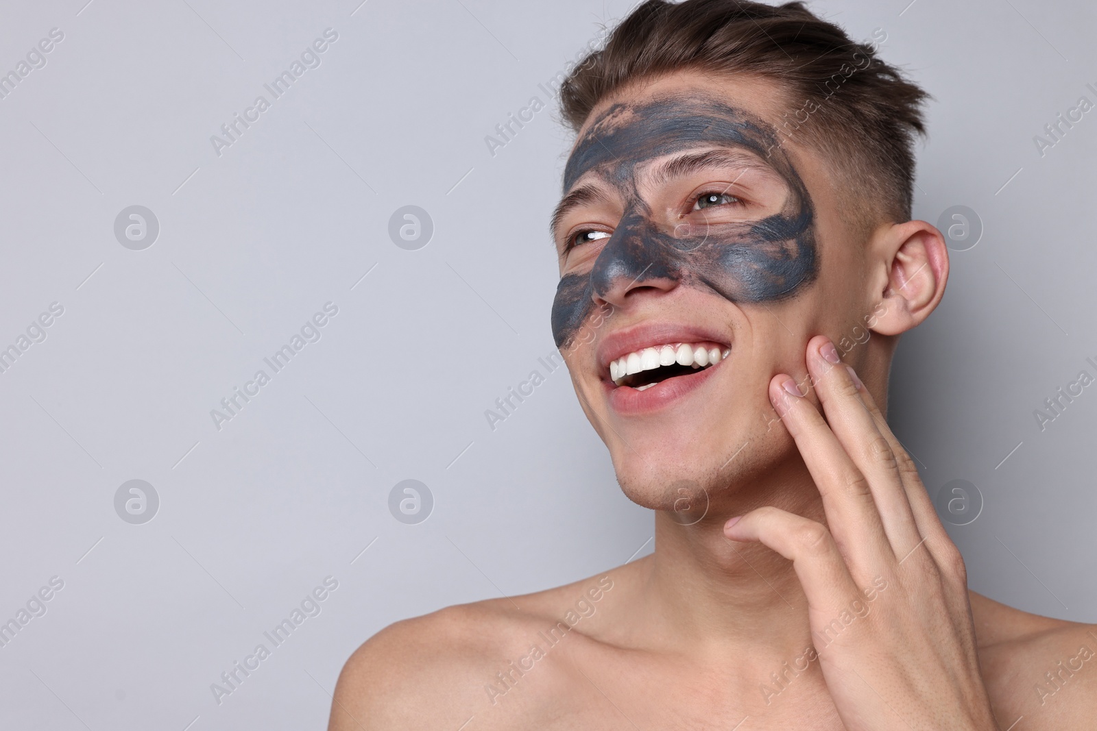 Photo of Handsome man with clay mask on his face against light grey background. Space for text